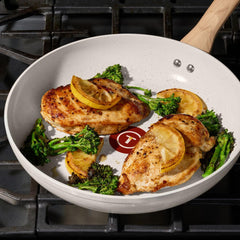 Two seasoned chicken breasts with lemon slices and broccoli cooking in a ceramic frypan