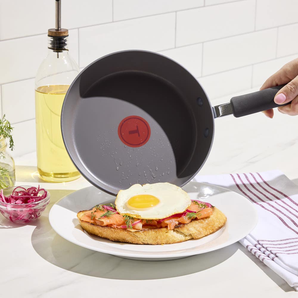 A nonstick frying pan placing a fried egg on toast with smoked salmon and herbs.
