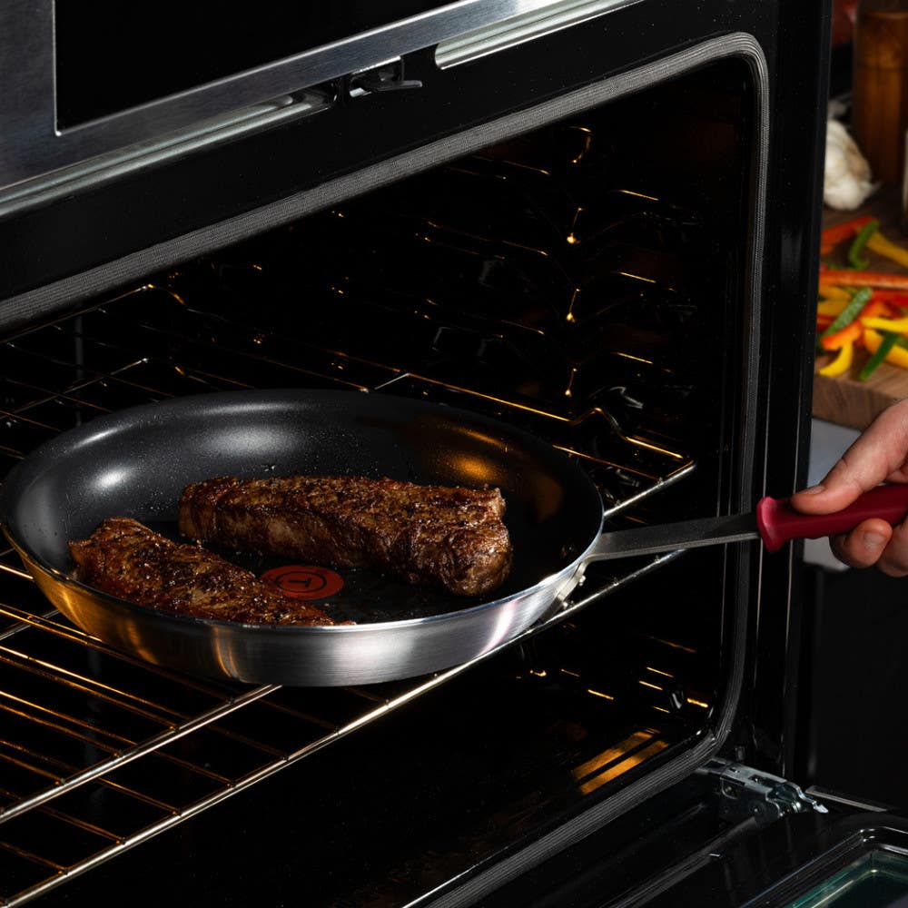 Hand placing a nonstick frypan with two seared steaks into oven