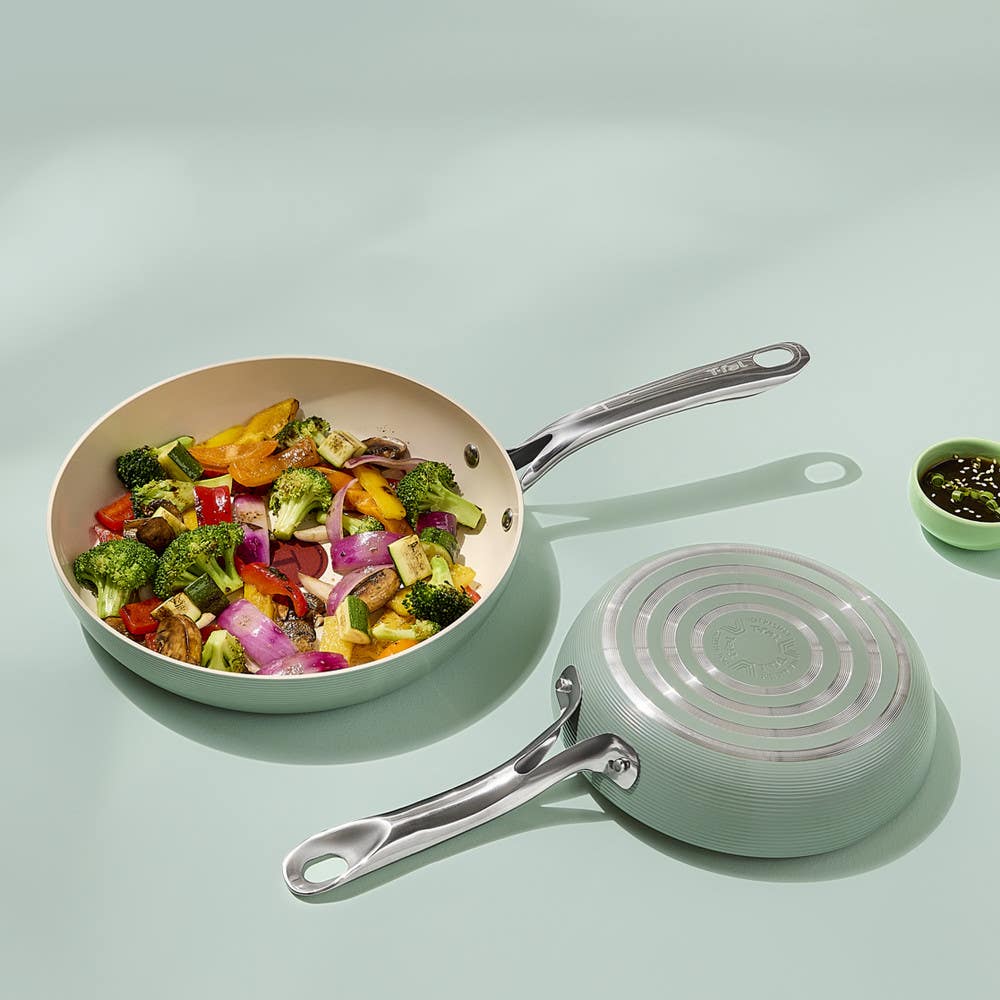 Two ceramic mint green frypans, one with sautéed vegetables, and one showing base on a light green surface.