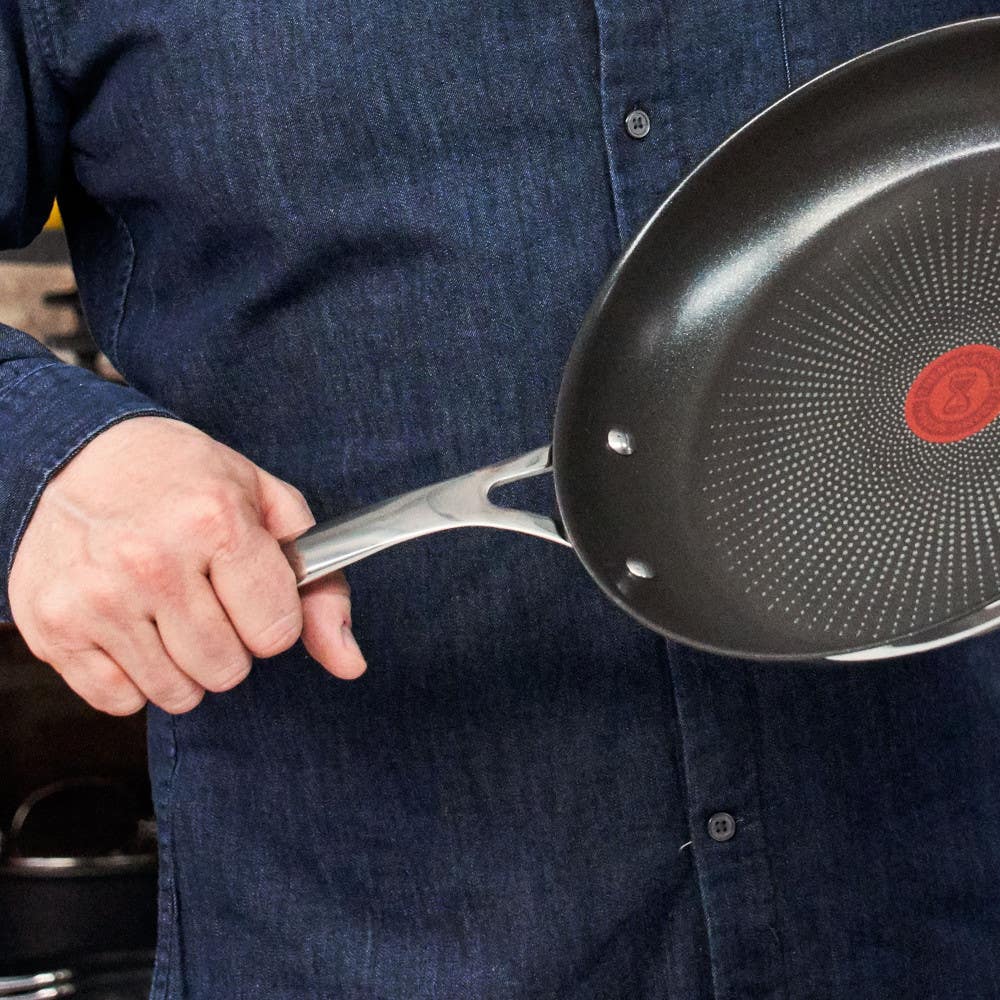 Man in denim shirt holding nonstick frypan with red heat indicator and stainless handle