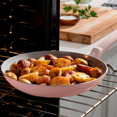 T-fal pink ceramic frypan with roasted potatoes resting on an oven rack in an open oven.
