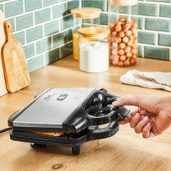Sandwich maker on a kitchen counter, being closed by a hand