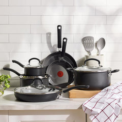 Set of black nonstick pots and pans with glass lids on a kitchen counter.