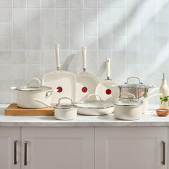 T-fal cream cookware set with nonstick frypans, pots and glass lids displayed on kitchen countertop with white tile wall