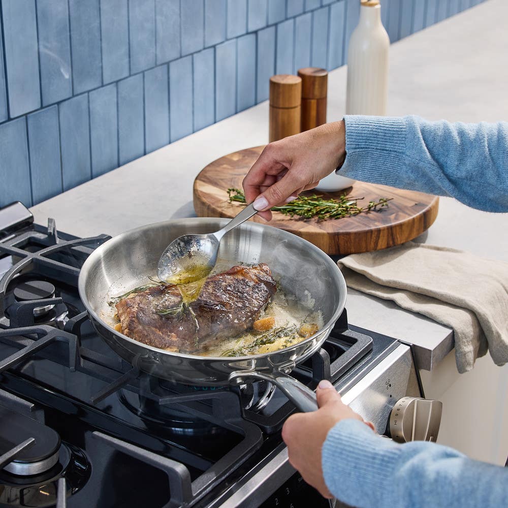 Hand basting steak in stainless steel skillet on gas stove with herbs and butter