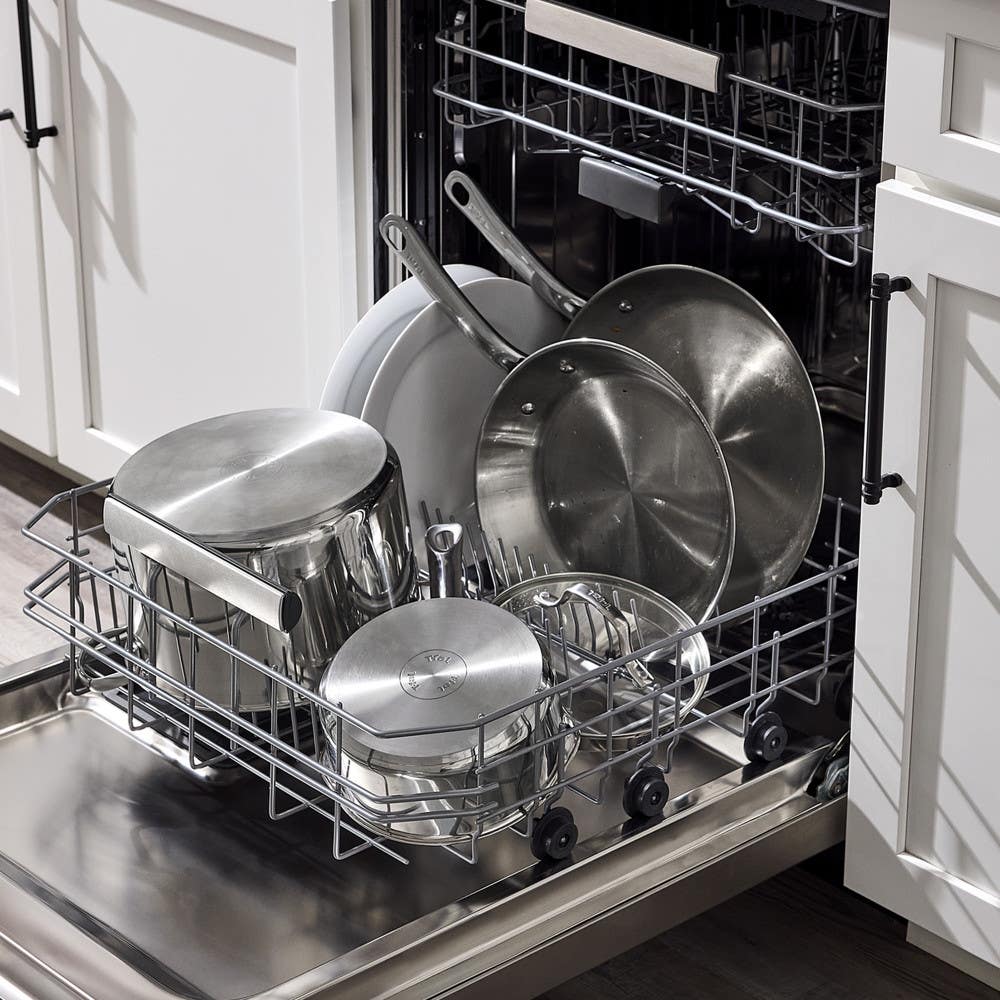 Open dishwasher loaded with stainless steel pots and pans.