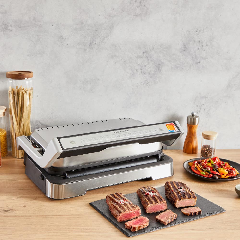 T-Fal OptiGrill on a kitchen counter alongside cooked steaks in different levels of doneness.