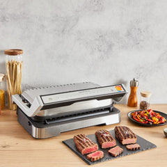 T-Fal OptiGrill on a kitchen counter alongside cooked steaks in different levels of doneness.