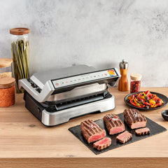 The OptiGrill in countertop alongside cooked meat in diffrent doneness levels.