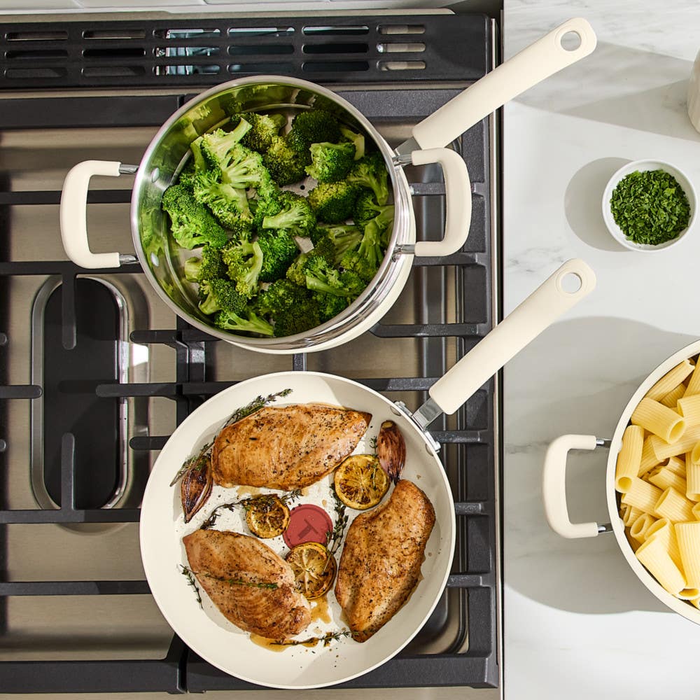 Overhead view of t-fal beige nonstick cookware cooking chicken, broccoli and pasta on gas cooktop
