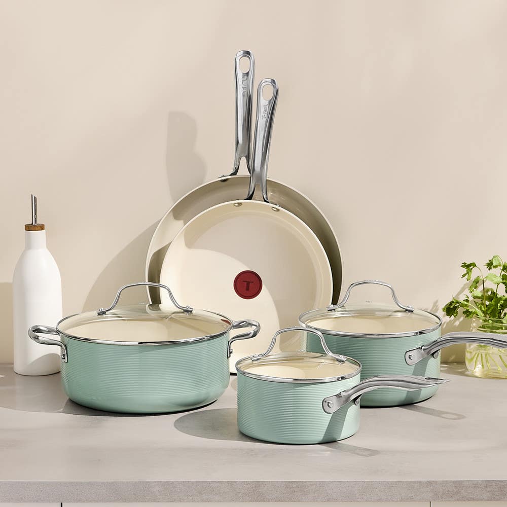 Set of mint green ceramic pots and pans with glass lids on a kitchen counter.