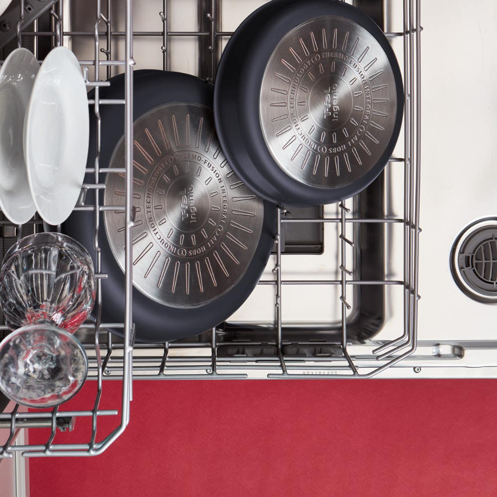Two black frying pans placed upside down in a dishwasher along with glass cups and plates