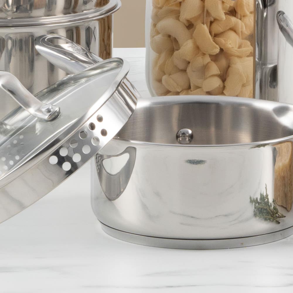Stainless steel saucepan with glass lid and pasta in a jar in the background.