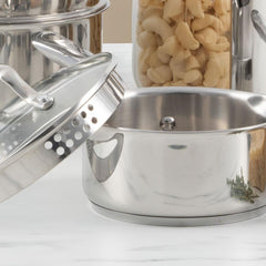 Stainless steel saucepan with glass lid and pasta in a jar in the background.