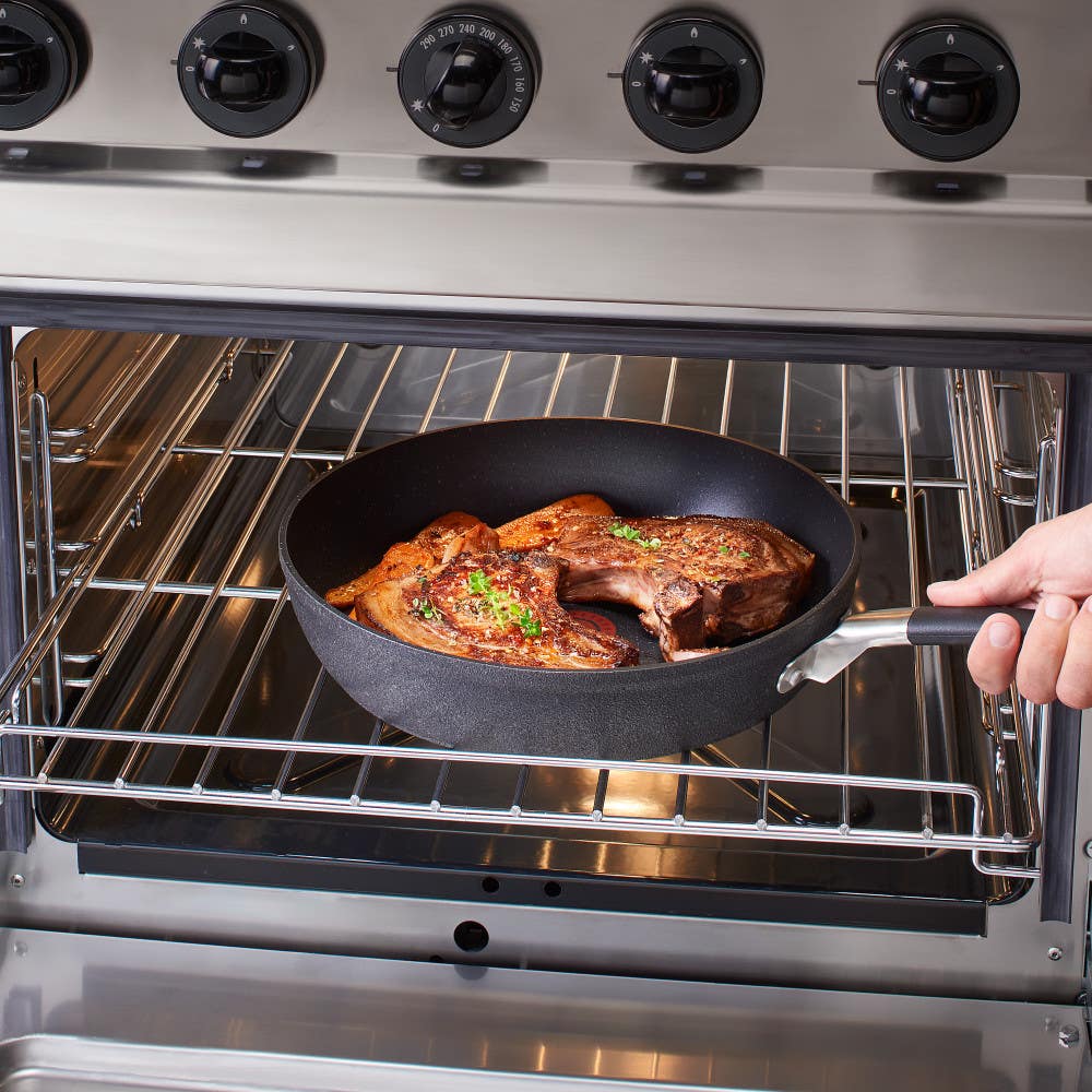 Stone Force Frying Pan with food cooking in an oven, held by a hand.