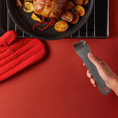 Black pan with roasted food, a red oven mitt, and a hand holding a grey detachable handle