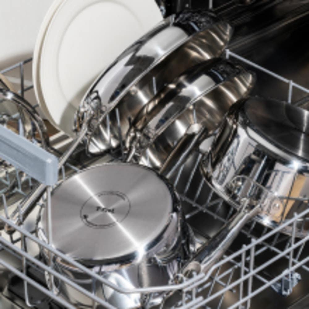 shiny stainless steel cookware and plates loaded in a dishwasher for cleaning