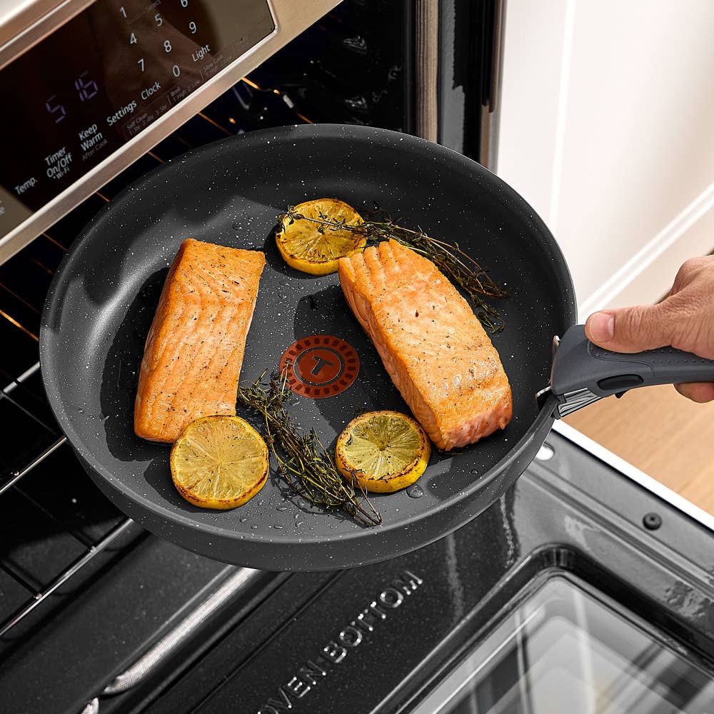 Hand placing a gray pan with salmon and lemons into an oven. Salmon is golden brown