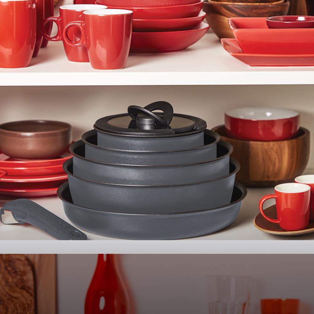 Stacked grey cookware among red and white dishware in a cabinet and a detachable handle