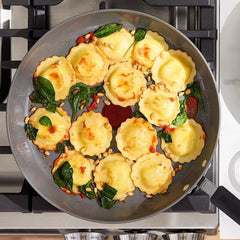 Ravioli with spinach and pine nuts in a ceramic skillet on a gas stovetop.
