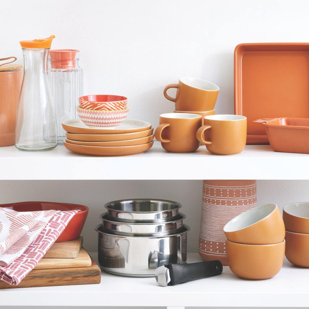Stacked stainless steel cookware surrounded by orange and brown dishware in a cabinet