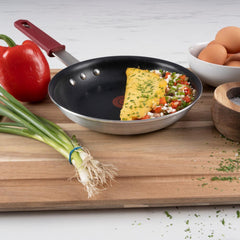 A nonstick frypan with a cooked omelette inside, amid vegetables and eggs on a wood board