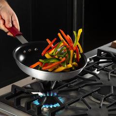 A person is sautéing colorful bell pepper strips in a nonstick frying pan over a gas stove