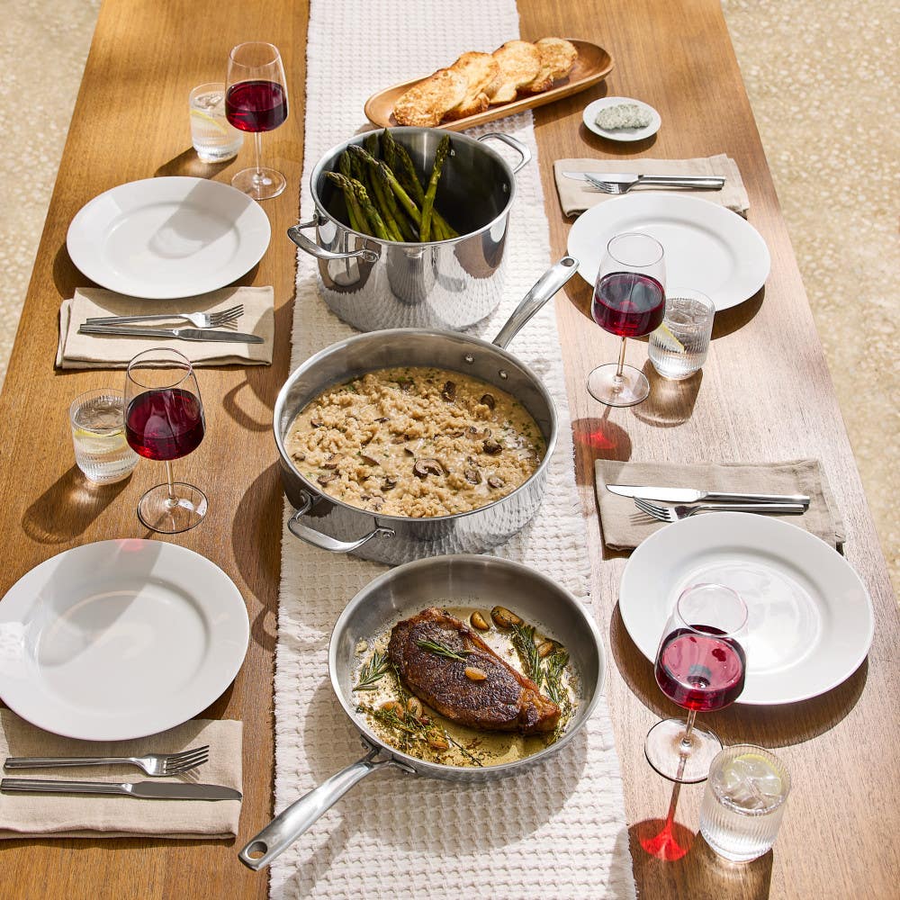 Wooden dining table elegantly set with stainless cookware serving fish, risotto and asparagus