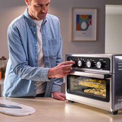 A person adjusts the T-fal air fryer in a modern kitchen. The fryer has food cooking inside