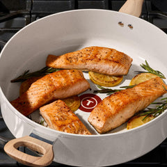 Salmon with lemon slices and rosemary cooking in a ceramic frypan