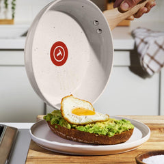 A beige with white dots ceramic frying pan serves a fried egg onto avocado toast.