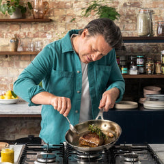 Chef searing steak with herbs in stainless frypan on stovetop in rustic kitchen