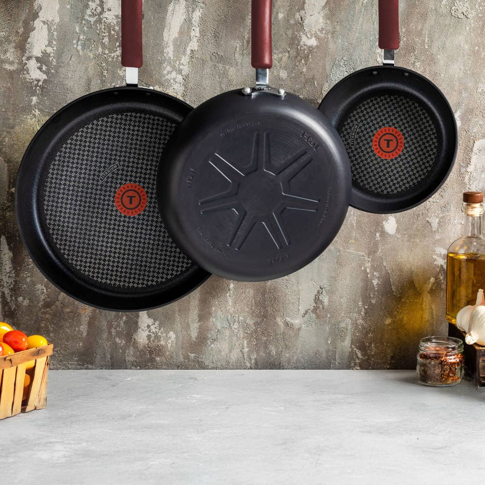 Three nonstick frying panswith red handles and red heat indicators hang on a kitchen wall.