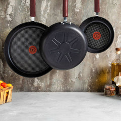 Three nonstick frying panswith red handles and red heat indicators hang on a kitchen wall.