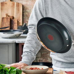 Man in gray sweater holding stainless nonstick frypan over counter with fresh veggies