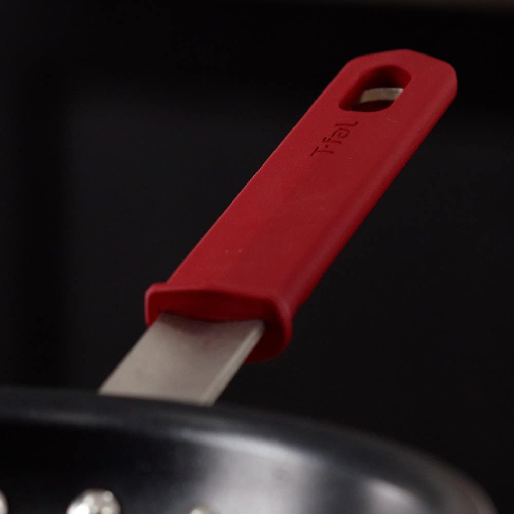 Close-up of red silicone sleeve protecting the stainless steel handle attached to a nonstick pan