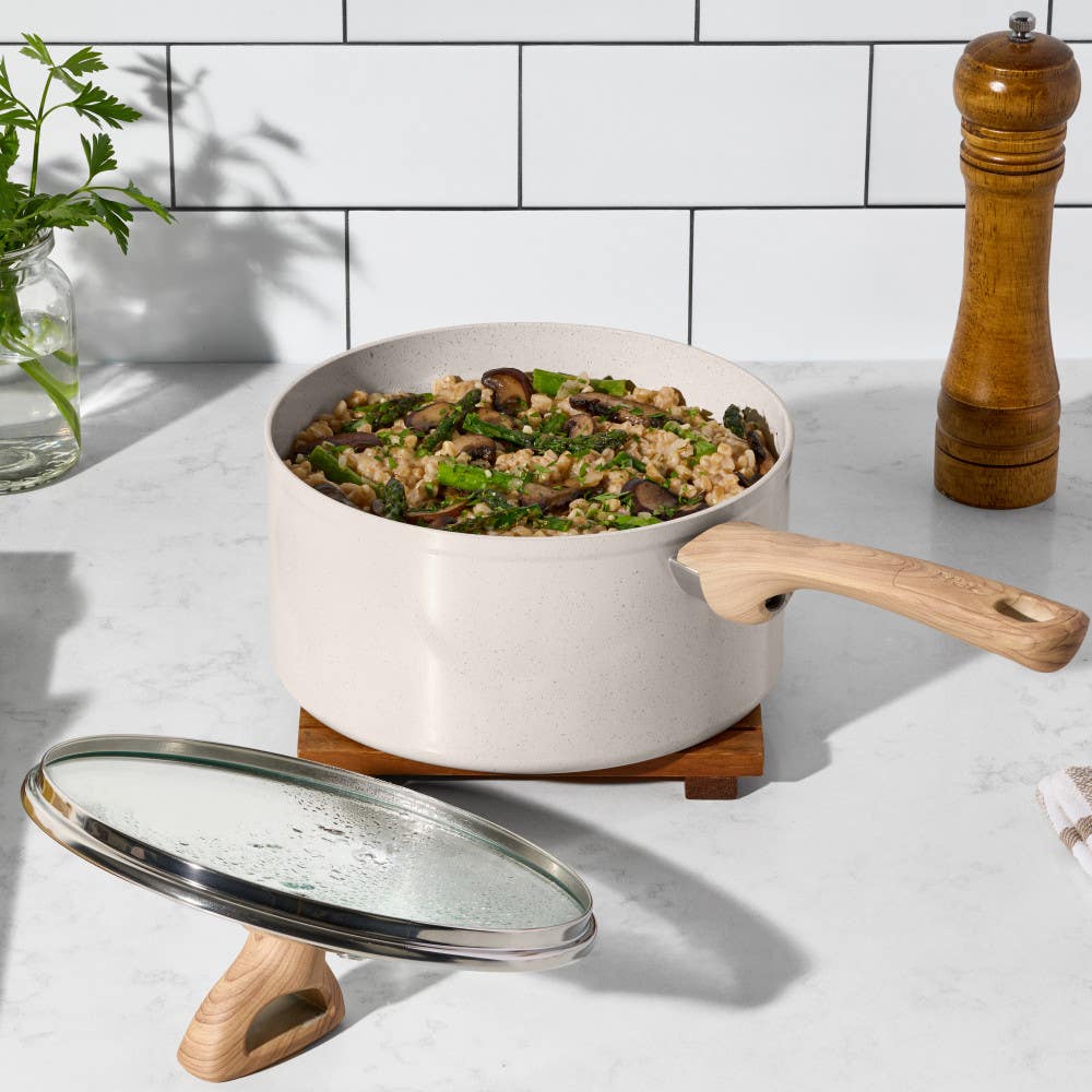 Beige ceramic saucepan with wooden handle, lid on stand, filled with lentils and vegetables