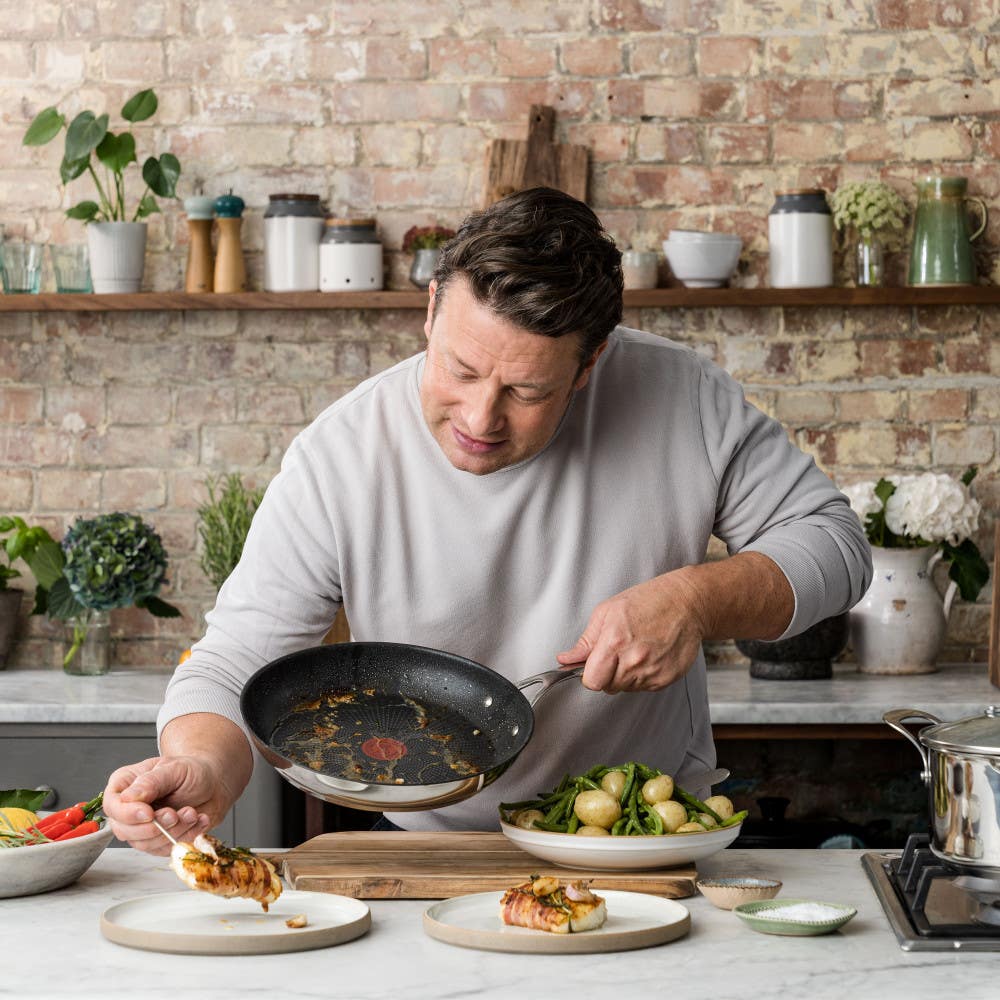 Chef serving food from a stainless steel nonstick frypan onto plated dishes on counter
