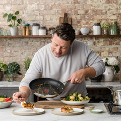 Chef serving food from a stainless steel nonstick frypan onto plated dishes on counter