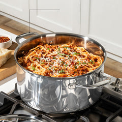 A stainless steel pot on a stove filled with spaghetti and sauce topped with herbs and cheese