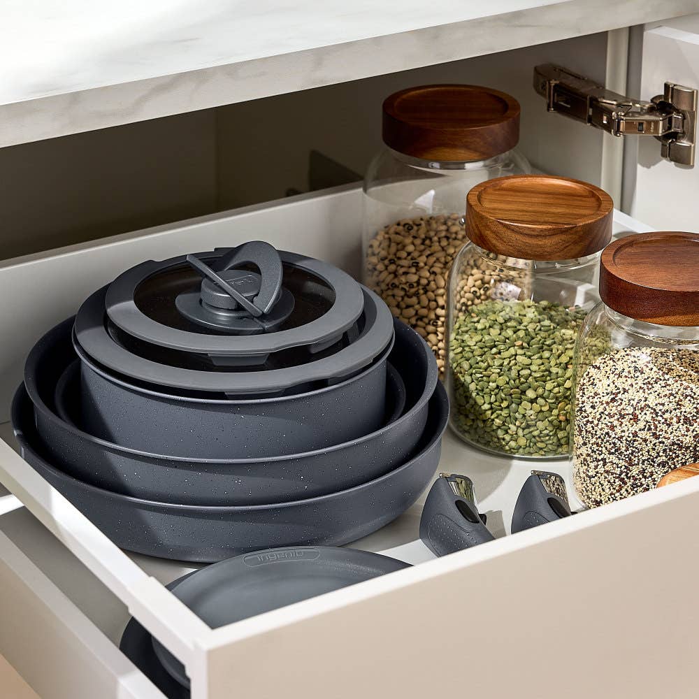 Stacked grey cookware in drawer surrounded by jars of grains, showcasing organized storage