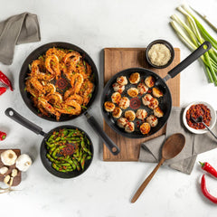 Overhead view of black nonstick pans with shrimp, dumplings, and green beans