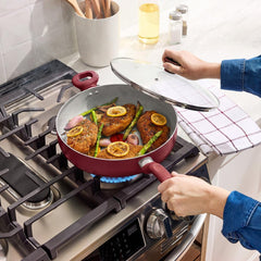 Hand lifting glass lid from red sauté pan with chicken and vegetables on gas stove