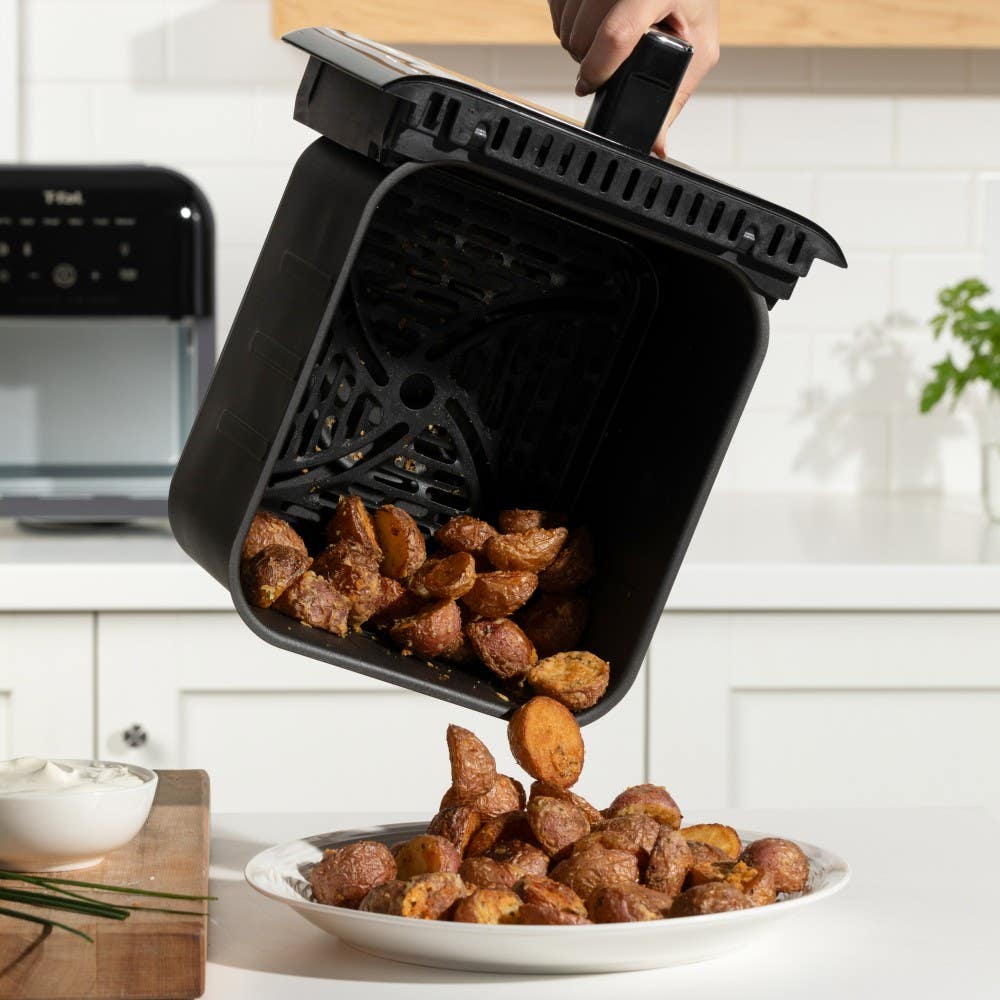 Hand pouring crispy roasted potatoes from the air fryer basket onto a plate