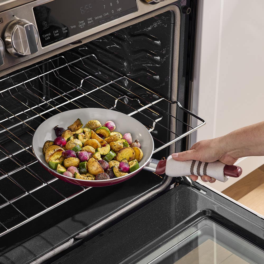 Red frying pan with roasted potatoes being removed from oven by hand
