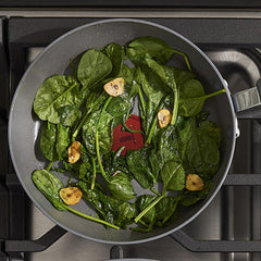 Fresh spinach and garlic slices sautéing in a nonstick frying pan on a gas stove.