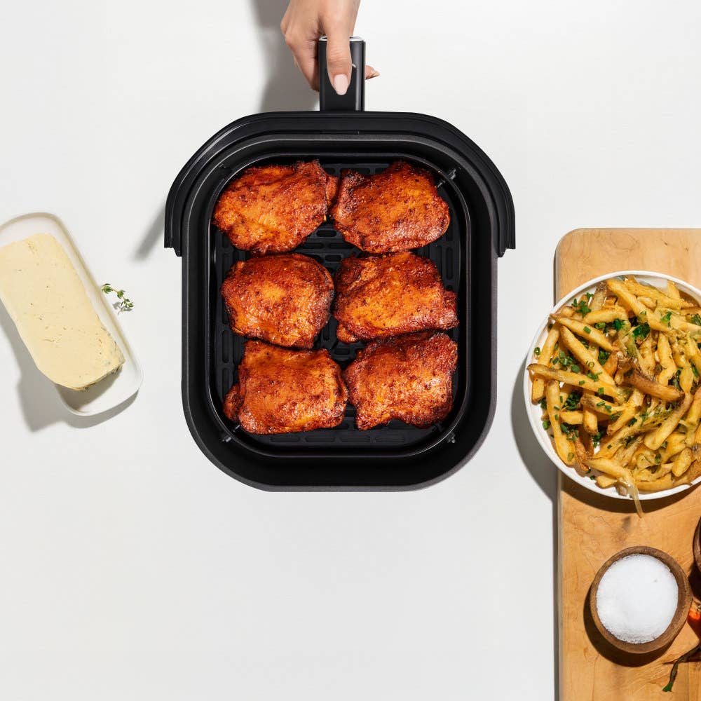 A hand holding an air fryer basket filled with six cooked chicken thighs, emphasizing its large 7L capacity.