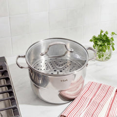 T-fal stainless steel steamer pot with glass lid and insert on counter, herbs in back