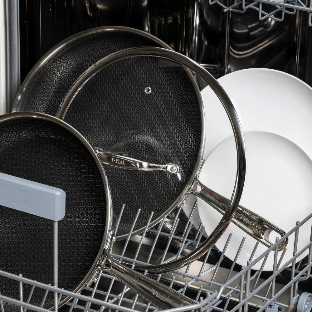 Stainless steel cookware and plates neatly arranged inside a dishwasher for cleaning.